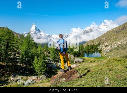 Wanderer steht auf Felsen und in die Ferne schaut, hinter dem See Grindij und Schnee - Matterhorn, Wallis, Schweiz abgedeckt Stockfoto