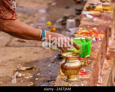 Eine Frau bereitet ein persönliches Angebot für einen Hindu Gottheit mit einer Messing Topf, ein Korb mit Betel Blätter und Früchte und bunte kumkum Pulver. Stockfoto