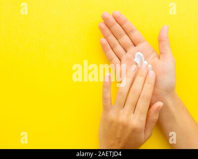 Frau Hände Anwendung Creme auf gelben Hintergrund mit Kopie Raum isoliert. Bild horizontal, Flach, Draufsicht von oben Stockfoto