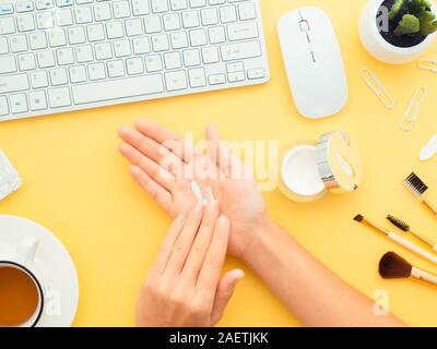 Praktische Anwendung der Creme am Arbeitsplatz. Frische, grüne Pflanze, Creme, Make-up-Pinsel, Tasse Kaffee, body Duschgel handgemachte Seife, Tastatur, Maus isoliert o Stockfoto