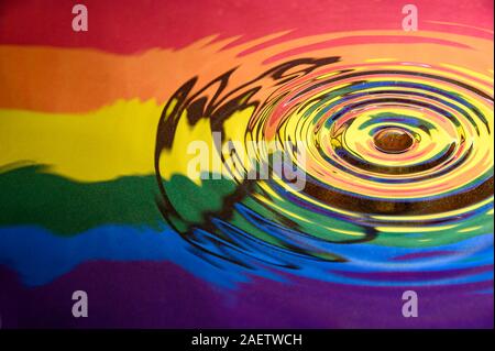 Off Center Spritzwasser und kreisförmigen Wellen auf der Oberfläche spiegelt die Gay Pride Aussterben Rebellion Fahne und Logo. Abstrakte Gay Pride Hintergrund Stockfoto