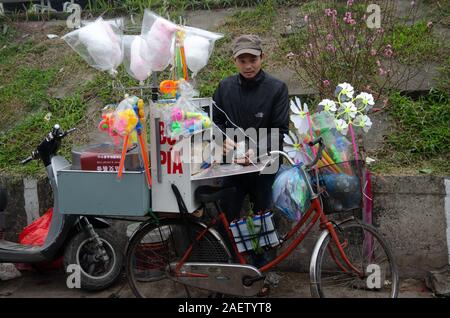 Einem Straßenhändler verkauft bò popiah Bía (süß), Zuckerwatte, und Spielzeug von seinem Fahrrad am Straßenrand stehen in Hanoi, Vietnam Stockfoto