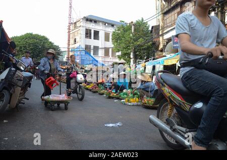 Straße Händler verkaufen Obst und Gemüse auf einem Markt in der Altstadt von Hanoi, Vietnam als Menschen, die zu Fuß und mit Motorrad fahren Stockfoto