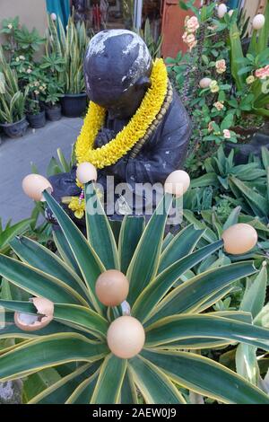 Eierschalen werden auf die Spitzen einer Anlage vor einer Statue eines Mannes in einem Garten in Bali, Indonesien beten setzen Stockfoto