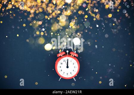 Silvester oder Weihnachten Zusammensetzung flache Ansicht von oben Xmas holiday Celebration rot Wecker mit goldenen Konfetti Lichter legen Bokeh auf schwarzem Hintergrund. Te Stockfoto