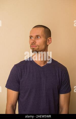 Ein attraktiver junger Mann im blauen T-Shirt stellt gegen eine beige Wand Stockfoto