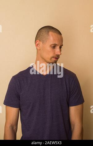 Ein attraktiver junger Mann im blauen T-Shirt stellt gegen eine beige Wand Stockfoto