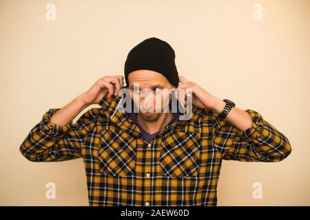 Junger Mann, Modell der Mode, trug einen karierten Hemd mit einem biege blind hinter ihm. Kerl in schwarzer Hut mit Bart im lässigen Stil Stockfoto