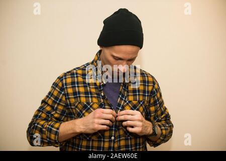 Junger Mann, Modell der Mode, trug einen karierten Hemd mit einem biege blind hinter ihm. Kerl in schwarzer Hut mit Bart im lässigen Stil Stockfoto