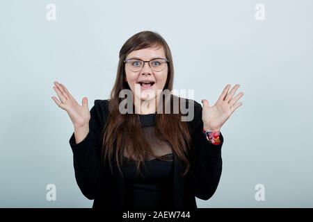 Junge Frau in Freizeitkleidung schockiert, steigende Hände, die Handflächen, lächelnd Stockfoto