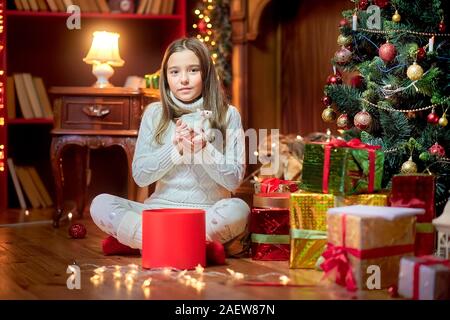 Süße kleine Mädchen sitzt auf dem Boden in der Nähe der Weihnachtsbaum hält in ihre Arme und Anschläge eine lustige weiße Ratte auf dem Hintergrund der helle Urlaub leuchtet. S Stockfoto