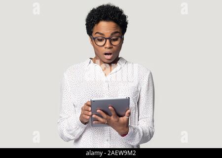 Schwarze Frau an Tablet Bildschirm mit geöffnetem Mund geschockt. Stockfoto