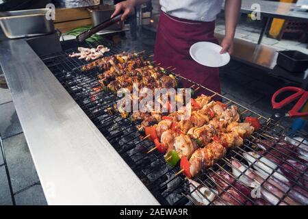 Auf dem Grill, eine Menge Fleisch gebraten am Spieß, der Koch dreht seine shish Kebabs. Hand eines Mannes, Pommes leckere Fleisch von Schwein am Spieß in Stockfoto