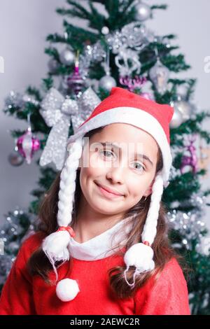 Portrait von Happy girl verkleidet als Weihnachtsmann neben dem Weihnachtsbaum. Stockfoto