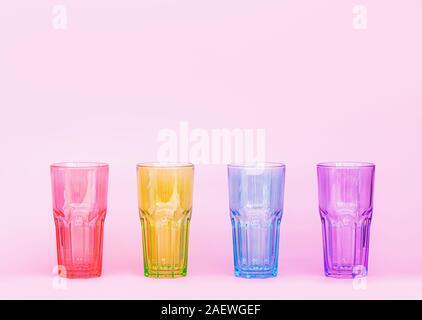 Mehrfarbige Gläser für Getränke auf einem rosa Hintergrund. Gläser aus Glas. Minimastic Komposition. Close Up. Stockfoto
