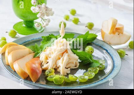 Traditionelle weiße weiche faserige Cecil Käse liegt auf einem blauen Platte. Käse ist mit Reifen Stachelbeeren und Süsse saftige Birne eingerichtet. Stockfoto