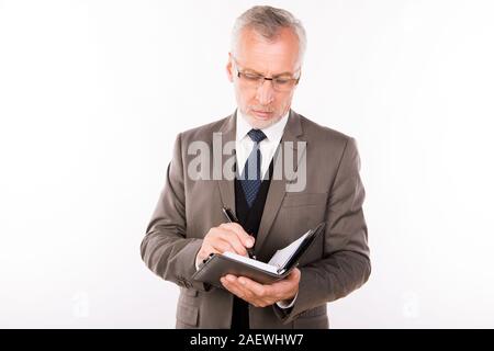 Alter Geschäftsmann in einem eleganten Anzug mit Brille Verfassen von Notizen Stockfoto