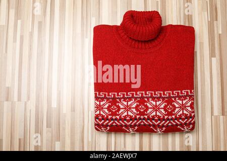 Rot gestrickt Weihnachten rollkragen pullover oder Pullover aus traditionellem Design mit weißen Skandinavischen geometrische Verzierung auf hölzernen Hintergrund gelegt gefaltet Stockfoto