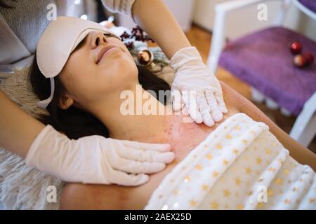 SPA Therapeut massiert Frau Brust mit Rosa scheuern. Therapeuten Hände mit Handschuhen schrubben Salt Scrub auf lächelnde Frau Brust in Schönheit cene Stockfoto