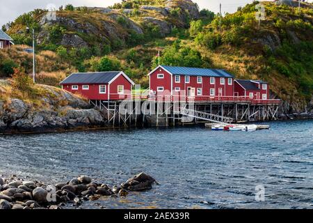 Eine rote Angeln Kabinen in Sakrisoy, einem kleinen Fischerdorf in Moskenes Gemeinde auf den Lofoten Inseln in Nordland County, Norwegen mit einem Berge in b Stockfoto