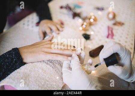 Prozess der Maniküre, Beauty Salon. Close-up Maniküre Hände in Weiß Latex Handschuhe arbeiten an Client Fingernägel auf Tabelle mit Weihnachten l Stockfoto