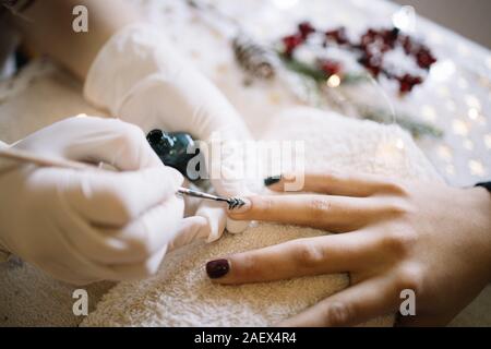 Frau mit Weihnachten Nagel Maniküre im Schönheitssalon. Nahaufnahmen der Hände tun, Weihnachtsbaum und Urlaub Maniküre auf die Nägel der Frau im SPA Salon, mit Stockfoto