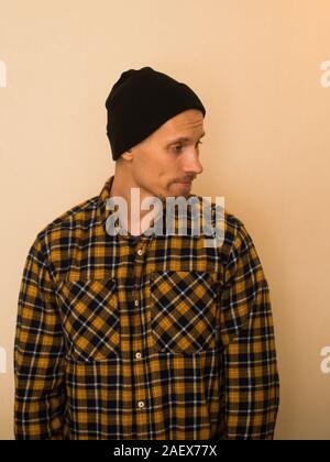 Junger Mann, Modell der Mode, trug einen karierten Hemd mit einem biege blind hinter ihm. Kerl in schwarzer Hut mit Bart im lässigen Stil. Stockfoto