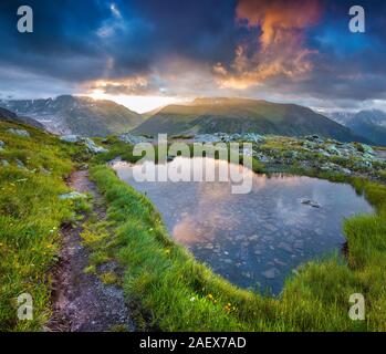 Dramatischer Himmel in kleinen See in den Schweizer Alpen wider. Sommer morgen Szene in der Nähe der Totensee auf dem Grimselpass. Alpen, Schweiz, Europa. Stockfoto