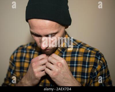Junger Mann, Modell der Mode, trug einen karierten Hemd mit einem biege blind hinter ihm. Kerl in schwarzer Hut mit Bart im lässigen Stil. Stockfoto