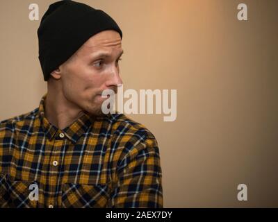 Junger Mann, Modell der Mode, trug einen karierten Hemd mit einem biege blind hinter ihm. Kerl in schwarzer Hut mit Bart im lässigen Stil. Stockfoto