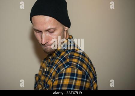Junger Mann, Modell der Mode, trug einen karierten Hemd mit einem biege blind hinter ihm. Kerl in schwarzer Hut mit Bart im lässigen Stil. Stockfoto