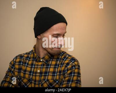 Junger Mann, Modell der Mode, trug einen karierten Hemd mit einem biege blind hinter ihm. Kerl in schwarzer Hut mit Bart im lässigen Stil. Stockfoto