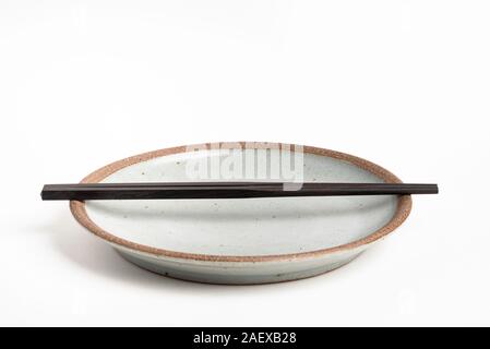 Ein paar orientalische schwarze hölzerne Stäbchen ruht auf einem strukturierten Steinzeug Platte und auf weißem Hintergrund. Stockfoto