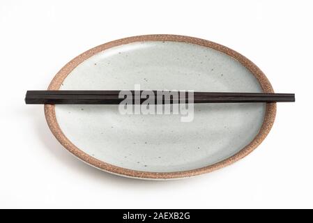 Ein paar orientalische schwarze hölzerne Stäbchen ruht auf einem strukturierten Steinzeug Platte und auf weißem Hintergrund. Stockfoto
