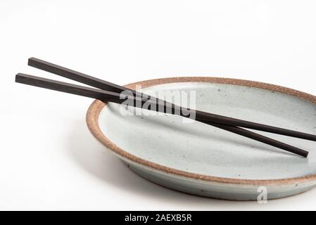 Ein paar orientalische schwarze hölzerne Stäbchen ruht auf einem strukturierten Steinzeug Platte und auf weißem Hintergrund. Stockfoto