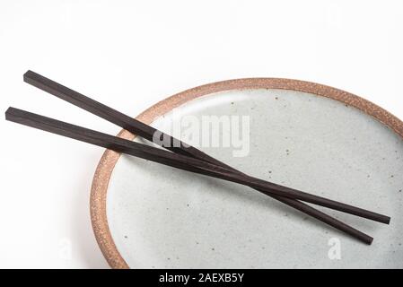 Ein paar orientalische schwarze hölzerne Stäbchen ruht auf einem strukturierten Steinzeug Platte und auf weißem Hintergrund. Stockfoto