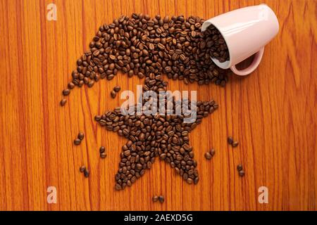 Verschüttete Kaffeebohnen aus der rosa Keramik Becher bilden ein Stern auf einer hölzernen Tisch. Hintergrund Konzept für Weihnachten Grußkarte, winter Morgen, Stockfoto