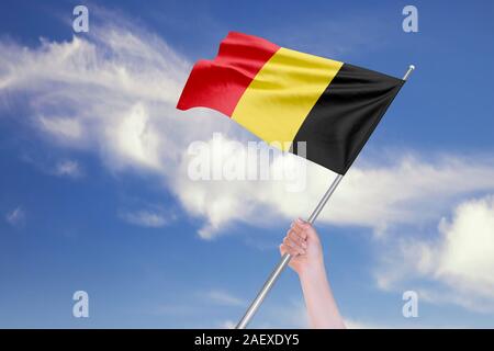 Weibliche hand winkt Belgien Flagge gegen den blauen Himmel mit Wolken. Realistische Spiegelungen und Texturen mit hoher Auflösung. 3D-Rendering. Stockfoto