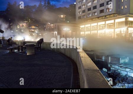 Touristen genießen den abendlichen Blick auf das schwefelhaltige Wasser am Heißwasserfeld (Yubatake) im Kusatsu Onsen Thermalbad in Gunma, Japan, Stockfoto