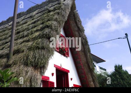 Weiße Fassade eines traditionellen Haus in Santana (Madeira) mit roten Fenstern und einem Strohdach (Portugal, Europa) Stockfoto