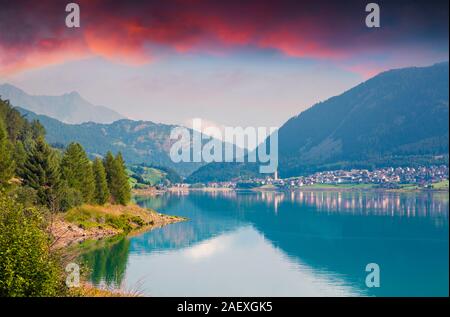 Dramatische Sommer Sonnenuntergang am Reschen See. Reschen Dorf im Morgennebel. Alpen, Europa. Stockfoto