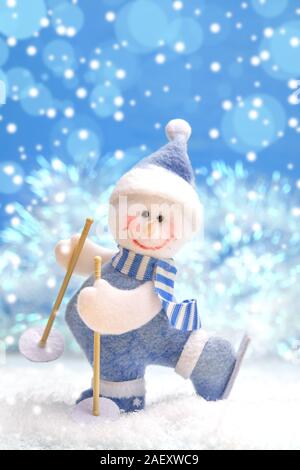Weihnachten Dekorationen. Spielzeug gefilzte Schneemann auf Skiern im Schnee auf Blau Weihnachten Hintergrund mit Bokeh. Stockfoto