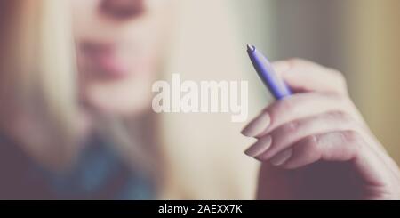 Weibliche Hand mit Stift in Luft auf lächelnde Gesicht Hintergrund, selektive konzentrieren. Stockfoto