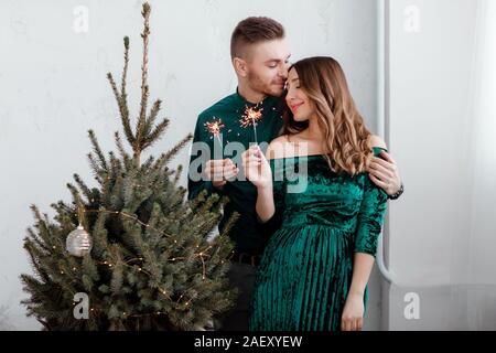 Brennende Wunderkerzen in den Händen der Partygäste. Paar Leute feiern Weihnachten und Feiertage glücklich in der Nähe der wunderschön geschmückten Weihnachtsbaum, ch Stockfoto