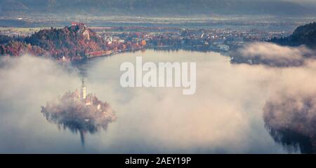 Luftaufnahme der Kirche der Himmelfahrt der Maria auf den Bleder See. Nebliger Herbst Landschaft in den Julischen Alpen, Slowenien, Europa. Stockfoto