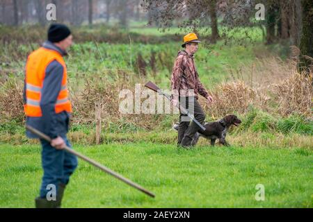 REUTUM, Niederlande - 07 Dez, 2019: Männer mit Schrotflinte und Sticks sind zu Fuß auf einer Linie in einem offenen Feld Jagd auf Hasen en Fasane. Stockfoto