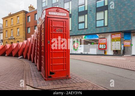 Eine Reihe von Schrägen iconic Telefonzellen in London mit einigen bunten Gebäude, das als Hintergrund. Stockfoto