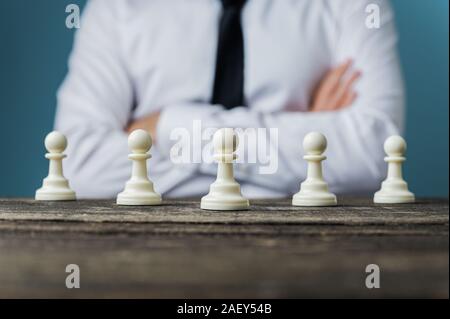 Geschäftsmann mit verschränkten Armen sitzt hinter einem Schreibtisch mit Schach schachfigur Stücke auf es in einem konzeptionellen Bild platziert. Stockfoto