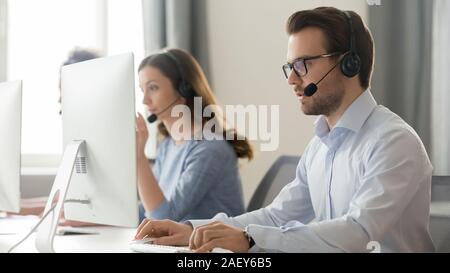 Männliche Mitarbeiter in Headset mit Mikrofon arbeiten am PC Stockfoto