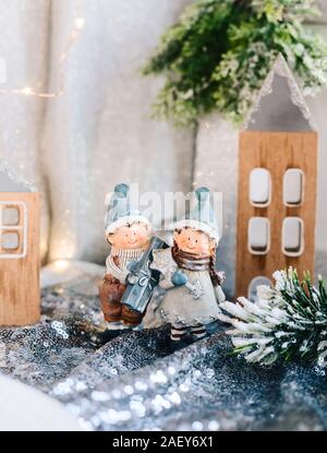 Porzellan Figuren der Kinder in eine weihnachtliche Dekoration. Winter Figuren der ein Junge und ein Mädchen mit den Geschenken, die auf dem Hintergrund der Häuser und Kegel. Weihnachten Stockfoto